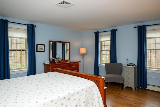 bedroom featuring visible vents, baseboard heating, and wood finished floors