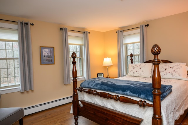 bedroom featuring wood finished floors, baseboard heating, and multiple windows