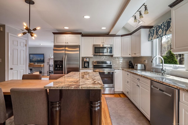 kitchen featuring appliances with stainless steel finishes, light stone counters, a sink, light wood finished floors, and backsplash