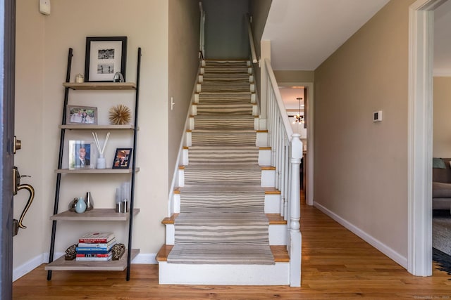 stairs featuring baseboards, wood finished floors, and an inviting chandelier