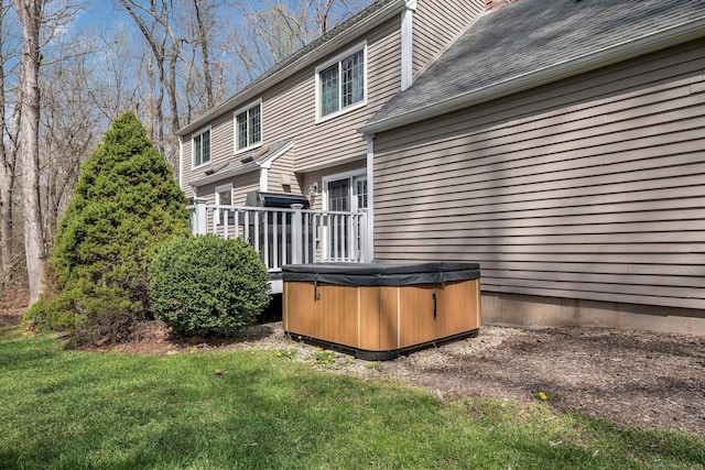 back of house with a hot tub, roof with shingles, and a yard