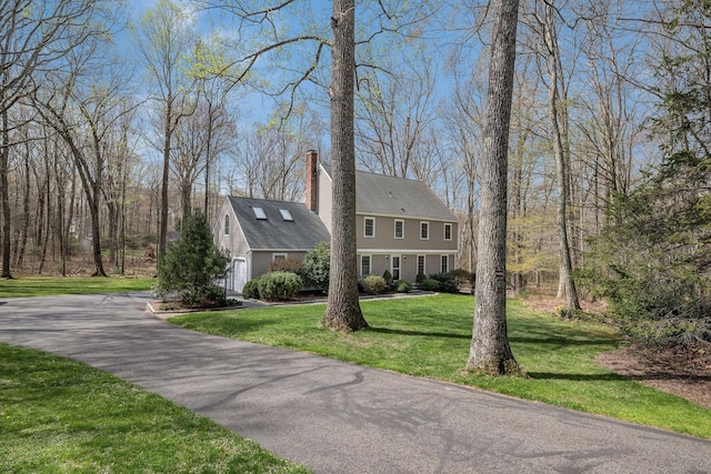 view of side of home featuring a yard, a garage, a chimney, and aphalt driveway