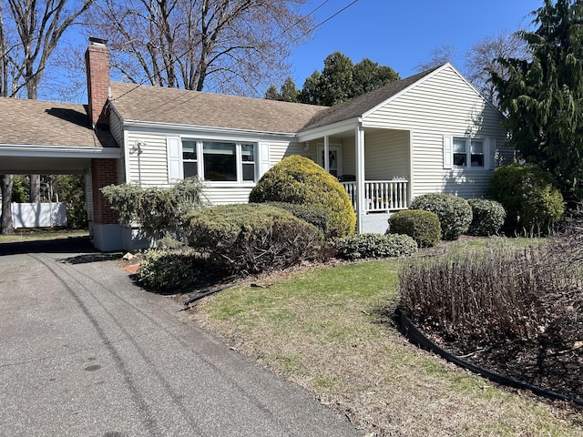 view of property exterior featuring a shingled roof, a porch, a chimney, an attached carport, and driveway