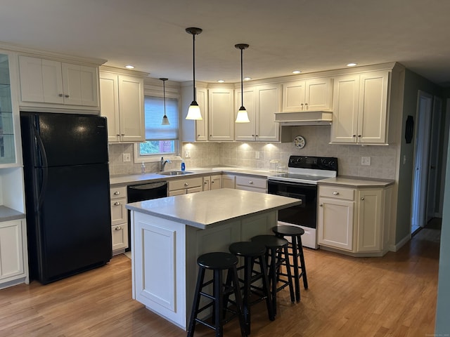 kitchen with light wood-type flooring, a kitchen breakfast bar, black appliances, under cabinet range hood, and a sink