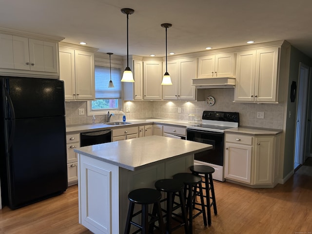 kitchen with a sink, light countertops, light wood-type flooring, under cabinet range hood, and black appliances
