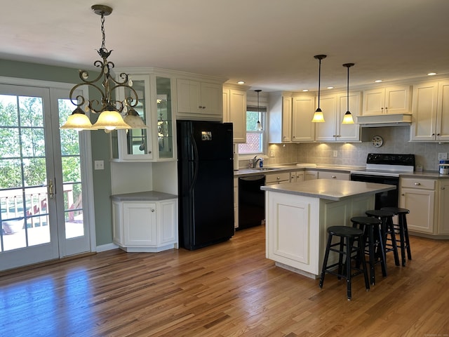 kitchen featuring glass insert cabinets, a sink, under cabinet range hood, black appliances, and light wood-style flooring