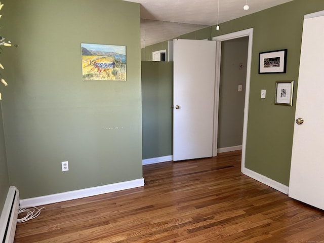 spare room featuring baseboards, a baseboard heating unit, and wood finished floors