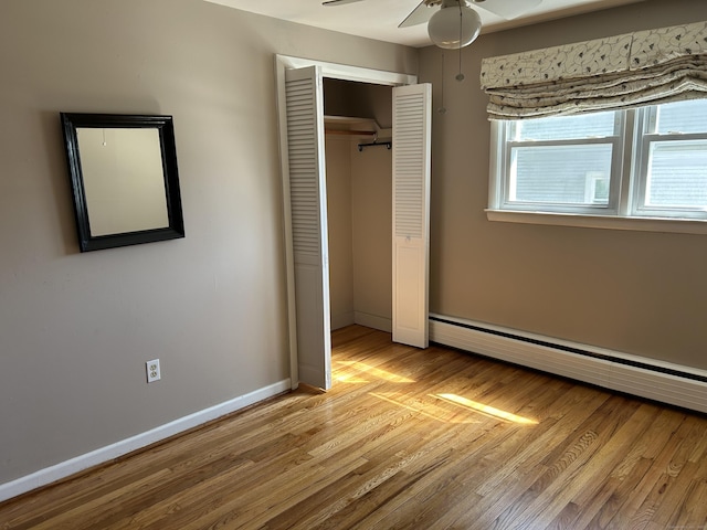 unfurnished bedroom with a closet, a baseboard radiator, light wood finished floors, and baseboards