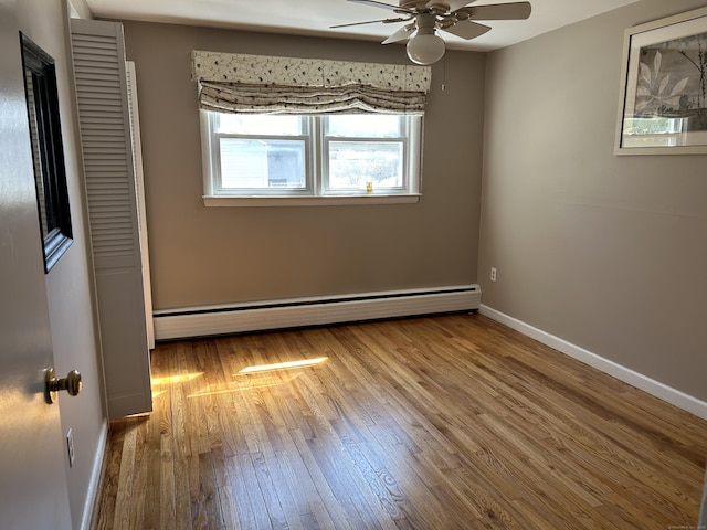empty room with baseboards, a ceiling fan, wood finished floors, and baseboard heating