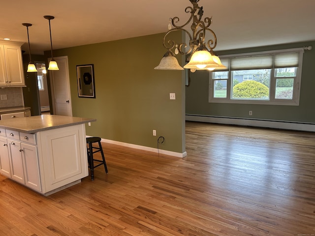kitchen with a baseboard radiator, a kitchen breakfast bar, white cabinetry, and wood finished floors