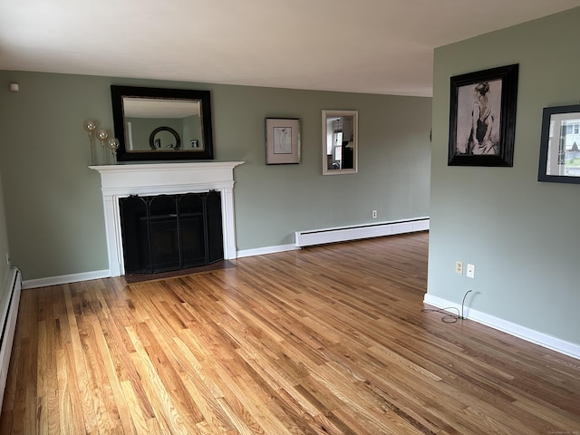 unfurnished living room featuring baseboard heating, a premium fireplace, baseboards, and wood finished floors