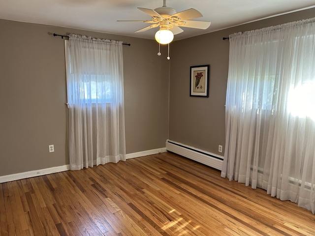 empty room featuring baseboards, a ceiling fan, a baseboard heating unit, and wood finished floors