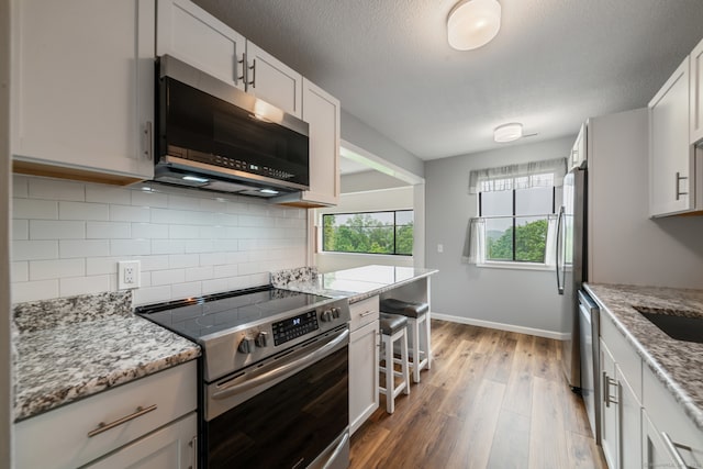 231 Heritage Vlg Unit C, Southbury, CT 06488 - kitchen featuring appliances with stainless steel finishes, light wood finished floors, backsplash, light stone countertops, and a textured ceiling