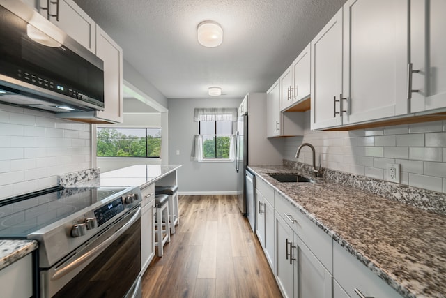231 Heritage Vlg Unit C, Southbury, CT 06488 - kitchen featuring stainless steel appliances, light wood finished floors, light stone counters, tasteful backsplash, and a textured ceiling