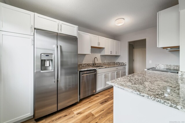 231 Heritage Vlg Unit C, Southbury, CT 06488 - kitchen with appliances with stainless steel finishes, light wood-style floors, white cabinets, light stone counters, and tasteful backsplash