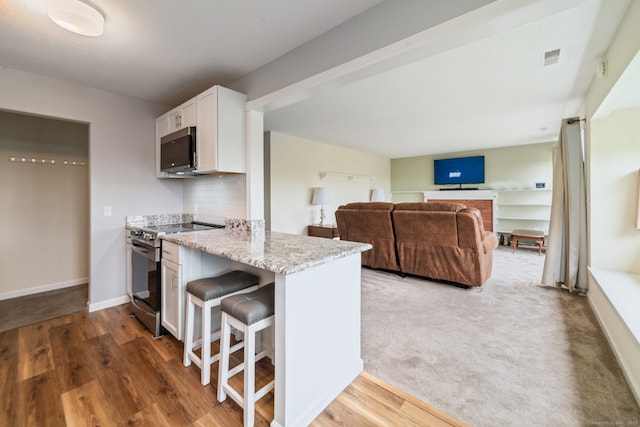 231 Heritage Vlg Unit C, Southbury, CT 06488 - kitchen featuring appliances with stainless steel finishes, light stone counters, white cabinetry, a breakfast bar, and a peninsula