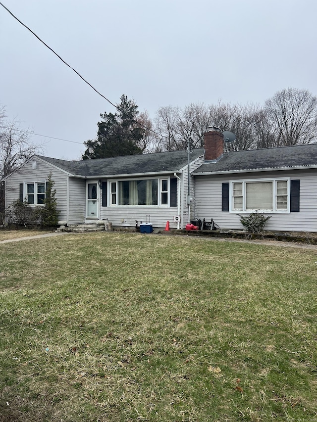 ranch-style home with entry steps, a chimney, a shingled roof, and a front yard