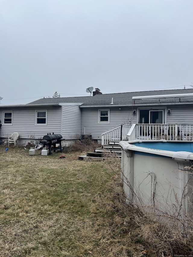 rear view of property with a shingled roof, an outdoor pool, a chimney, and a lawn