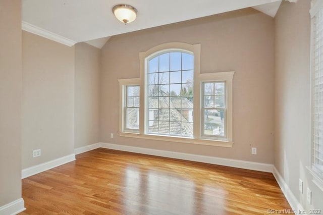 empty room with wood finished floors, baseboards, ornamental molding, and lofted ceiling