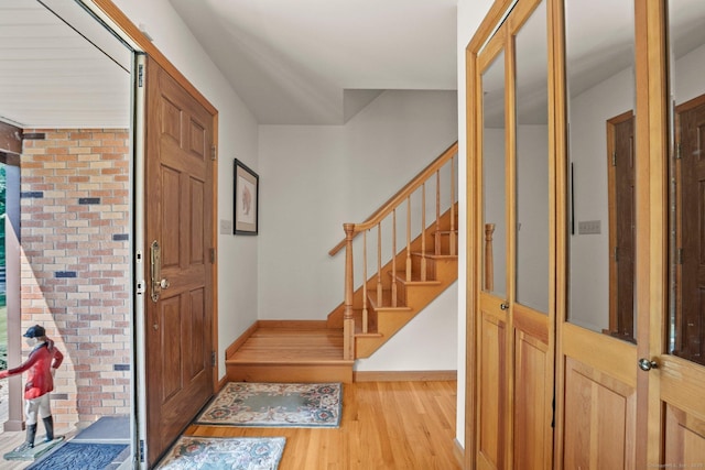 entrance foyer featuring brick wall, wood finished floors, baseboards, and stairway