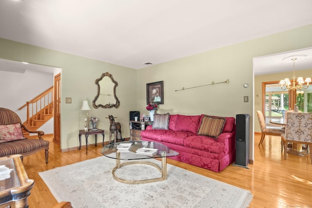 living room with wood finished floors, an inviting chandelier, baseboards, and stairway