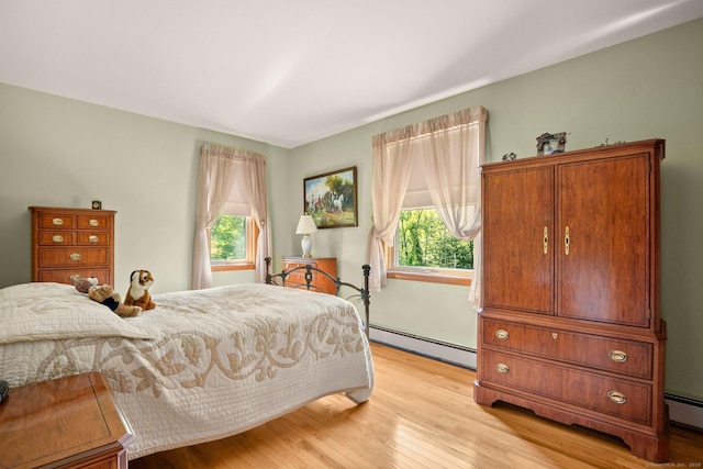 bedroom featuring light wood finished floors, multiple windows, and baseboard heating