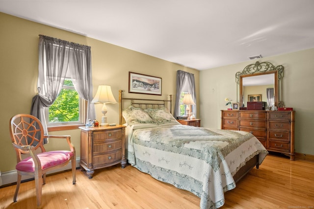 bedroom featuring light wood-style flooring, a baseboard heating unit, baseboards, and visible vents