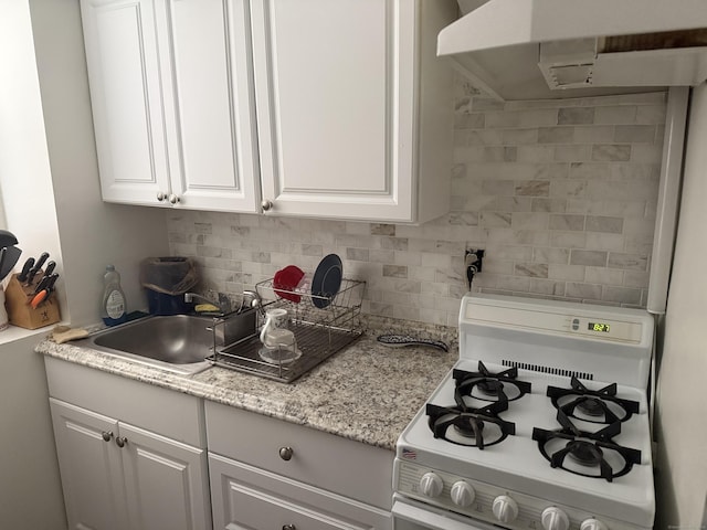 kitchen featuring white gas range, decorative backsplash, a sink, under cabinet range hood, and white cabinetry