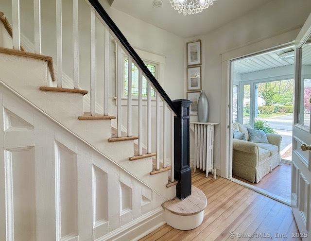 staircase featuring wood-type flooring, a notable chandelier, and radiator heating unit