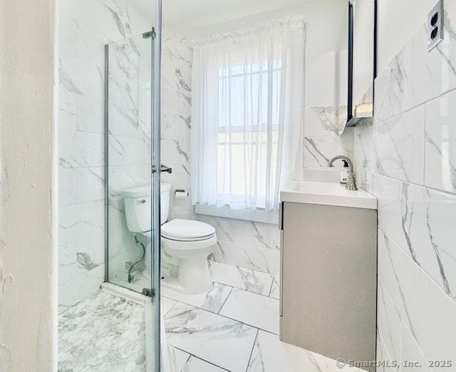 full bath with toilet, tile walls, a marble finish shower, and vanity