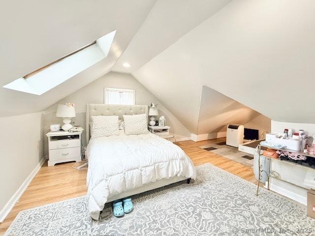 bedroom with baseboards, wood finished floors, and lofted ceiling with skylight