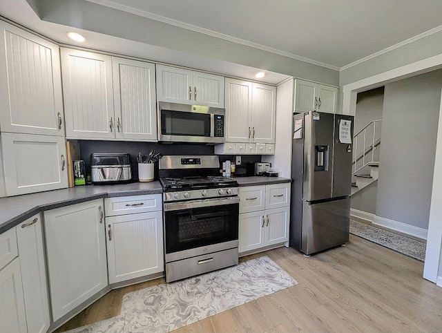 kitchen with baseboards, crown molding, dark countertops, appliances with stainless steel finishes, and light wood finished floors