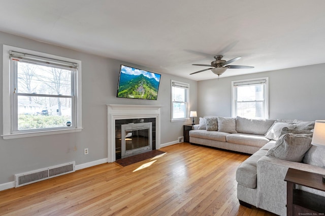 living area featuring baseboards, light wood-type flooring, a ceiling fan, visible vents, and a tile fireplace