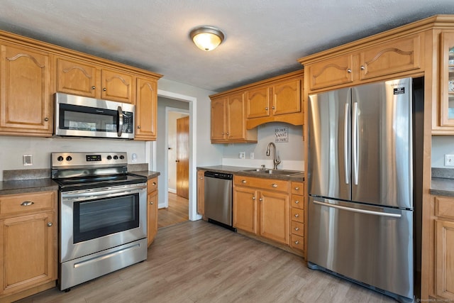 kitchen featuring light wood-style flooring, dark countertops, brown cabinets, stainless steel appliances, and a sink