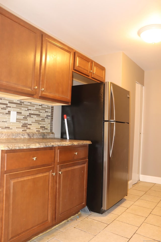 30 Woodland St Unit 5B, Hartford, CT 06105 - kitchen with light tile patterned floors, baseboards, freestanding refrigerator, brown cabinetry, and decorative backsplash
