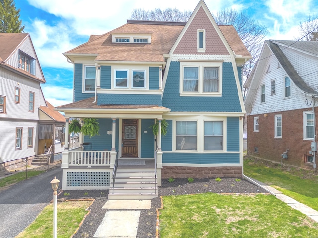 view of front of property featuring a porch, roof with shingles, and a front lawn
