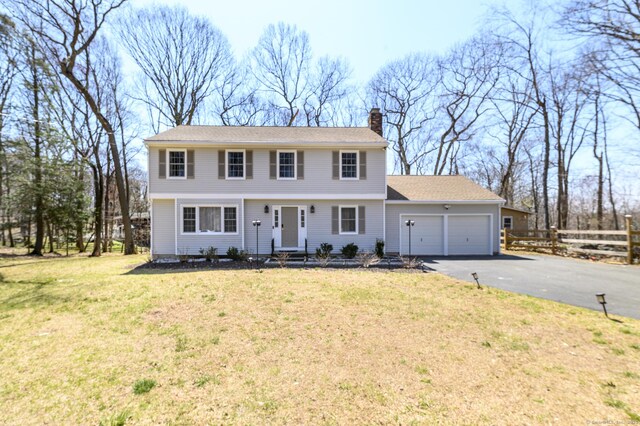 colonial home with a front lawn, a chimney, fence, an attached garage, and aphalt driveway