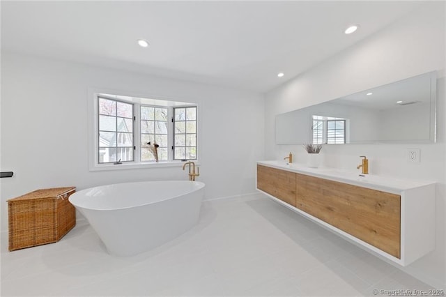 full bath featuring double vanity, baseboards, a freestanding bath, and recessed lighting