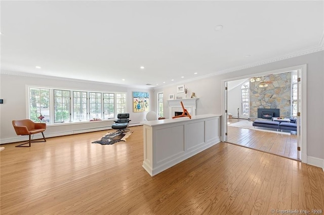 kitchen with ornamental molding, light wood-type flooring, a warm lit fireplace, and open floor plan