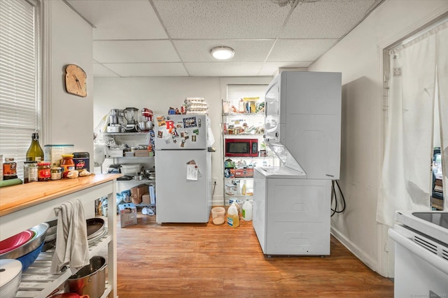 kitchen featuring light wood-style floors, stacked washer / dryer, a drop ceiling, and freestanding refrigerator