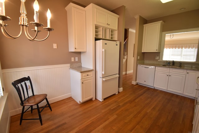 kitchen with a sink, white appliances, a chandelier, wood finished floors, and a wainscoted wall
