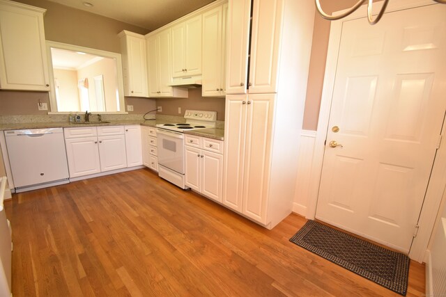 kitchen with white appliances, white cabinets, under cabinet range hood, light wood-style floors, and a sink
