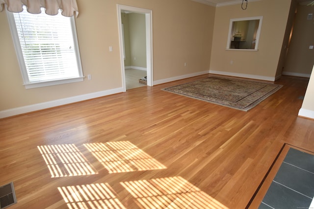 unfurnished living room with crown molding, visible vents, baseboards, and wood finished floors