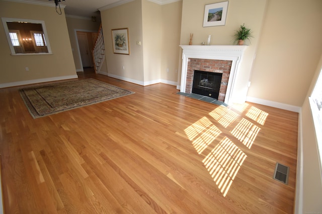 unfurnished living room with light wood-type flooring, a fireplace, crown molding, stairs, and visible vents