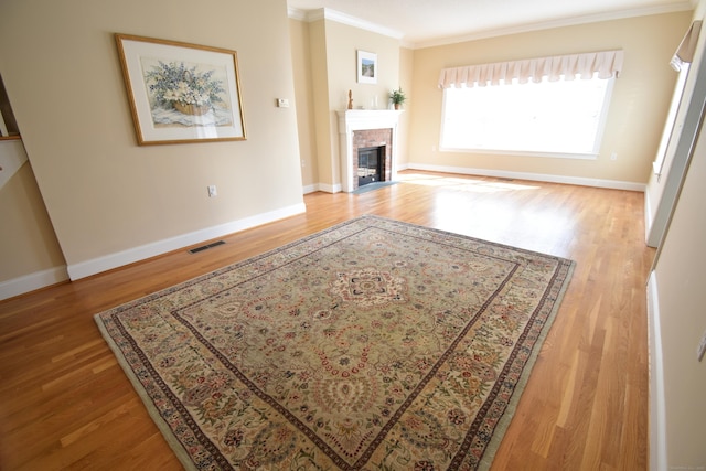 living room featuring crown molding, a fireplace with flush hearth, visible vents, wood finished floors, and baseboards