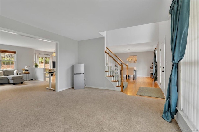 carpeted foyer entrance with a chandelier, baseboards, and stairs