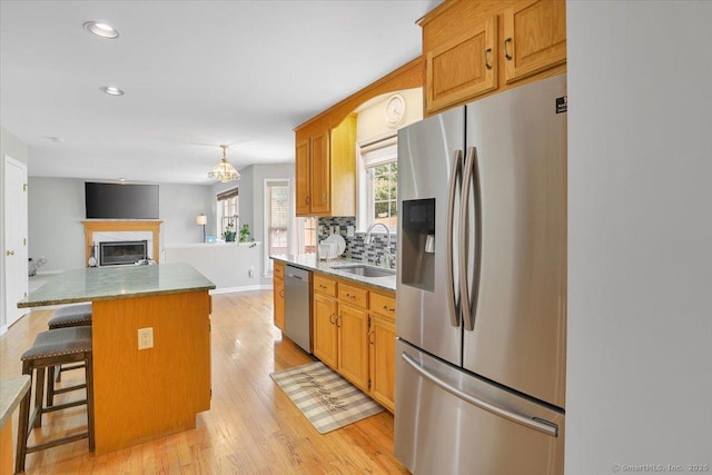 kitchen with light wood-type flooring, a center island, backsplash, stainless steel appliances, and a sink