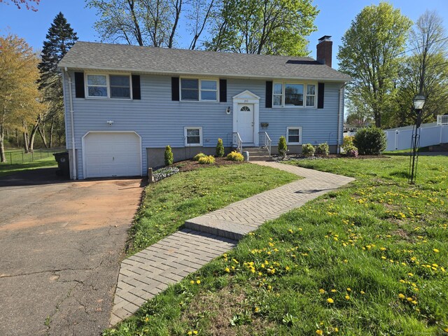 raised ranch with a front lawn, fence, a chimney, and concrete driveway
