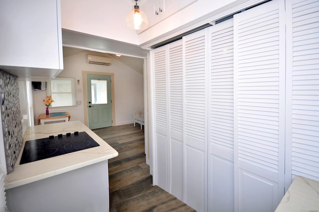 300 Mile Creek Rd, Old Lyme, CT 06371 - kitchen featuring a wall unit AC, black electric stovetop, dark wood finished floors, lofted ceiling, and light stone counters
