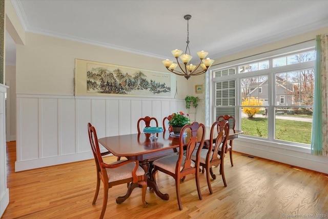 dining space featuring a chandelier, crown molding, light wood finished floors, a wainscoted wall, and a decorative wall
